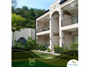 Un edificio de dos pisos con balcones, rodeado de vegetación y una piscina.
