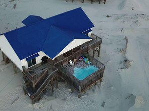 Una propiedad frente a la playa con piscina, terraza de madera y zona cubierta con sombrillas.