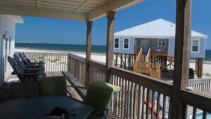 A covered deck with outdoor seating, overlooking a beach and a house with a white roof. - Island Time II - 102 Raphael S (Dauphin Island)