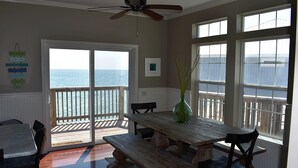 A dining area with a view of the ocean, a ceiling fan, and a wooden table with chairs. - Island Time - 103 Treasure Ct (Dauphin Island)
