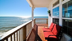 A wooden deck with a red bench and a potted plant, overlooking a calm sea. - Island Time - 103 Treasure Ct (Dauphin Island)