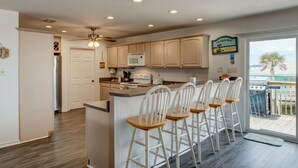 A kitchen with wooden cabinets, a microwave, and a bar area with stools. - Sandbar - 105 Raphael Semmes (Dauphin Island)