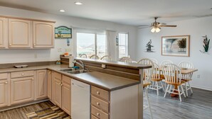 A kitchen with wooden cabinets, a dishwasher, and a dining area with white chairs and a wooden table. - Sandbar - 105 Raphael Semmes (Dauphin Island)