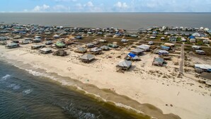An aerial view of a coastal area with numerous small buildings, some with attached docks, and a sandy beach. - Sandbar - 105 Raphael Semmes (Dauphin Island)