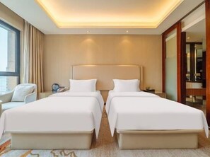 Habitación de hotel con dos camas, un rincón de estar con una silla y un ventanal grande.