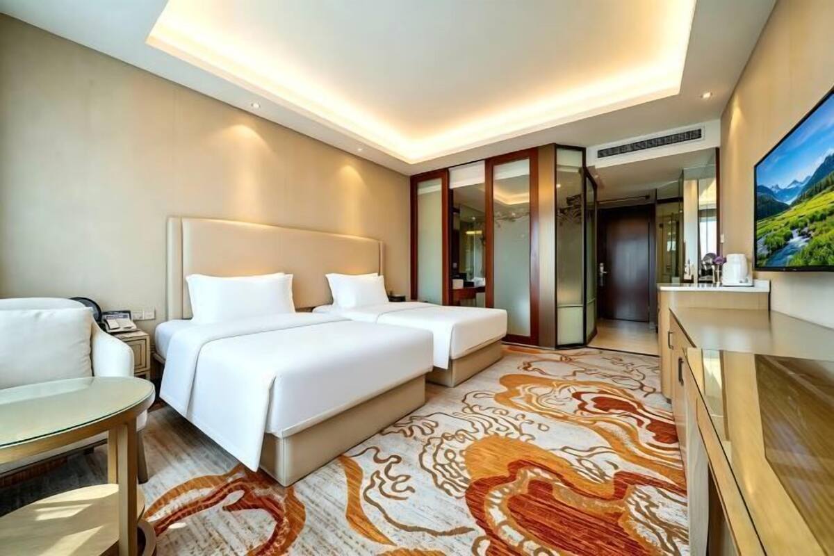 Une chambre d’hôtel avec deux lits, un bureau, une chaise, une télévision et une grande fenêtre.