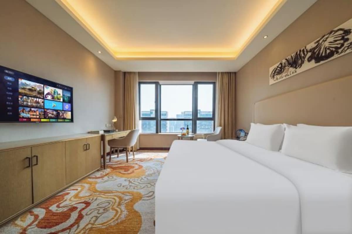 Een hotelkamer met een groot bed, een bureau, een stoel, een televisietoestel en een raam met uitzicht op de stad.
