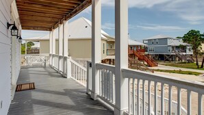 A covered porch with white railings, wooden beams, and a view of adjacent houses.