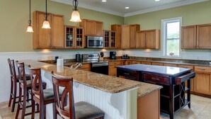 A kitchen with wooden cabinets, granite countertops, a central island with bar stools, and pendant lighting.