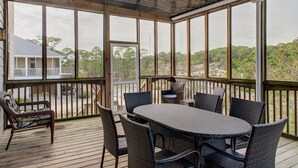 A covered outdoor area with a table and chairs, large windows, and a view of trees and a distant building.