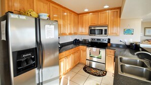 A modern kitchen with wooden cabinets, stainless steel appliances, and a checkered rug. - Second Wind - 2612 Bienville Blvd (Dauphin Island)