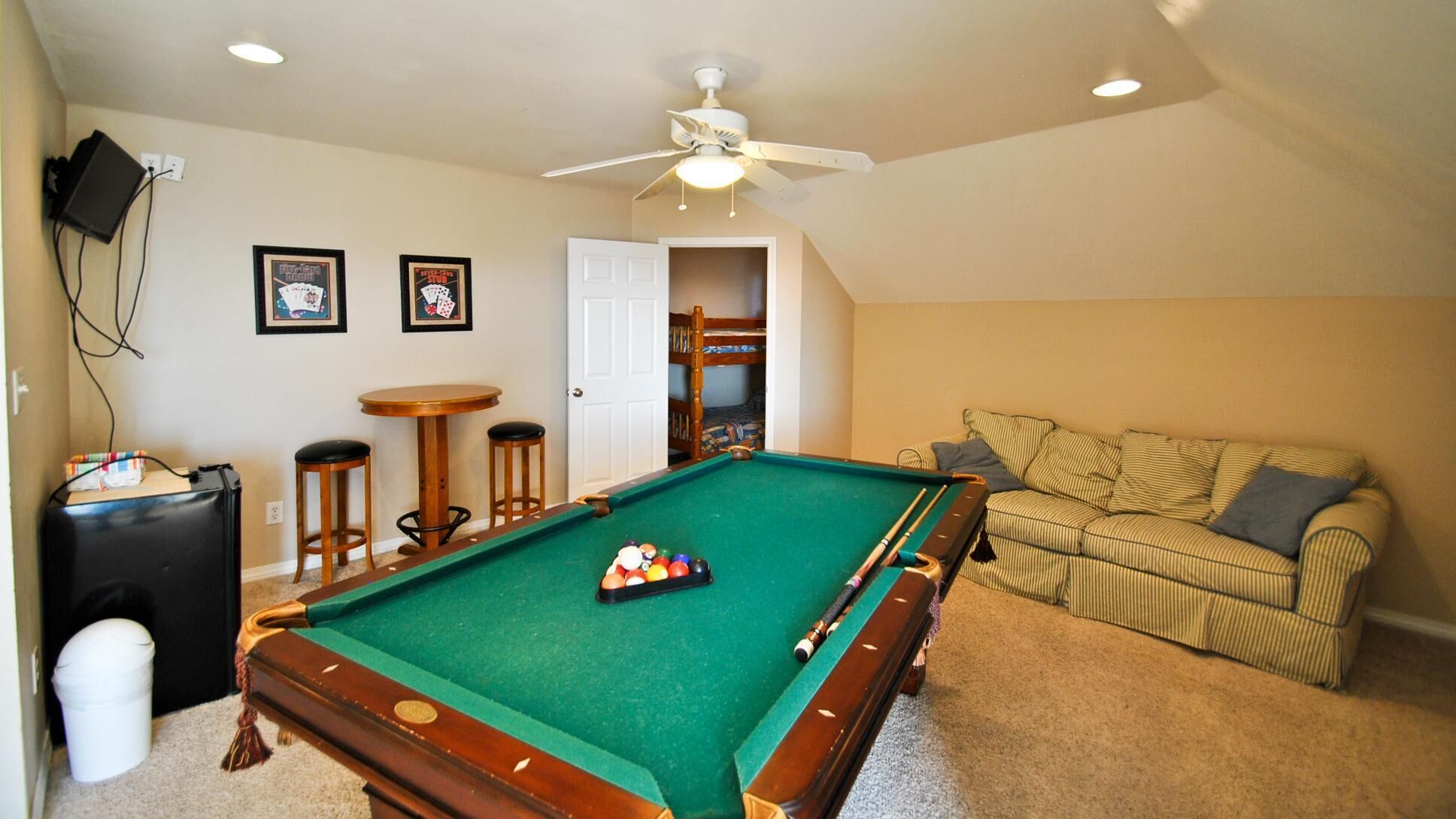 A pool table in a room with a ceiling fan, a couch, and a door leading to a bunk bed.