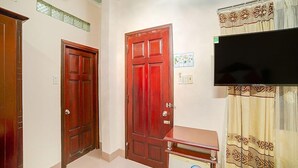 Um quarto com duas portas de madeira, uma mesa pequena com uma televisão e uma cortina com padrão decorativo.