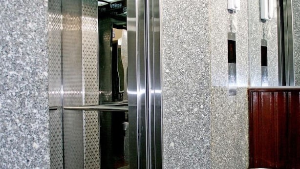 Interior de elevador com paredes metálicas e chão espelhado.