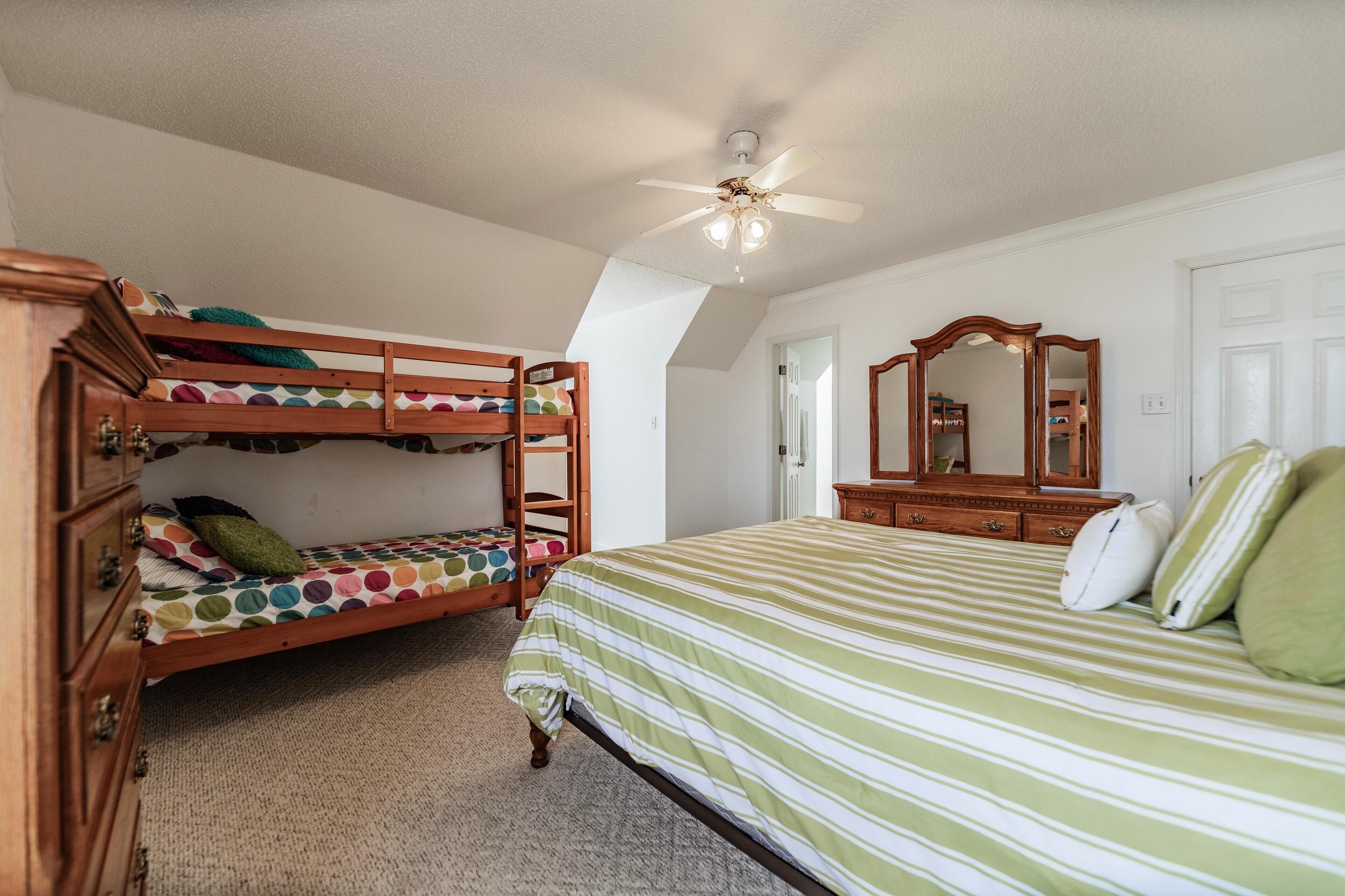 A bedroom with bunk beds, a single bed, a dresser, a mirror, and a ceiling fan.
