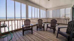 Una terraza de madera con sillas y una mesa, con vista a la playa.