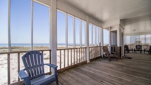 Una terraza de madera con vista a la playa, una silla Adirondack azul y una mesa con sillas.