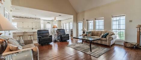 A spacious living room with hardwood flooring, a ceiling fan, and a large window providing natural light.