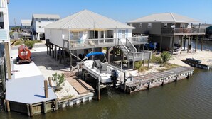 A waterfront property with a dock, a covered boat, and a house with a balcony. - Water's Edge - 2227 Mallard (Dauphin Island)
