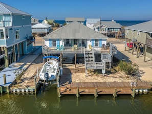 A waterfront property with a dock, a boat, and a house with multiple decks and outdoor seating. - Water's Edge - 2227 Mallard (Dauphin Island)