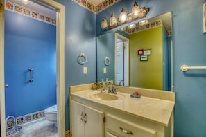 A bathroom with a blue wall, a beige vanity with a sink, a mirror, and a toilet. - Water's Edge - 2227 Mallard (Dauphin Island)