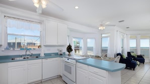 A spacious kitchen with white cabinets, a large island, and a view of the ocean. - Simple Pleasures - 103 Strand (Dauphin Island)