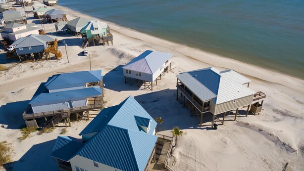 A coastal area with multiple beach houses featuring blue roofs and wooden structures. - Simple Pleasures - 103 Strand (Dauphin Island)