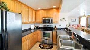 A modern kitchen with wooden cabinets, stainless steel appliances, a microwave, oven, and a sink. - Kowabunga - 102 Shell Ct (Dauphin Island)