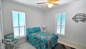 A bedroom with a bed, two windows with blinds, a ceiling fan, a bedside lamp, and a wall art piece. - West Beach - 104 Westward Ho (Dauphin Island)