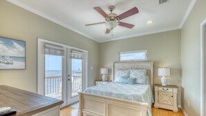 A bedroom with a bed, two bedside tables, a ceiling fan, and a view of the ocean through a sliding door. - Villa Delphinus - 103 Vargus C (Dauphin Island)
