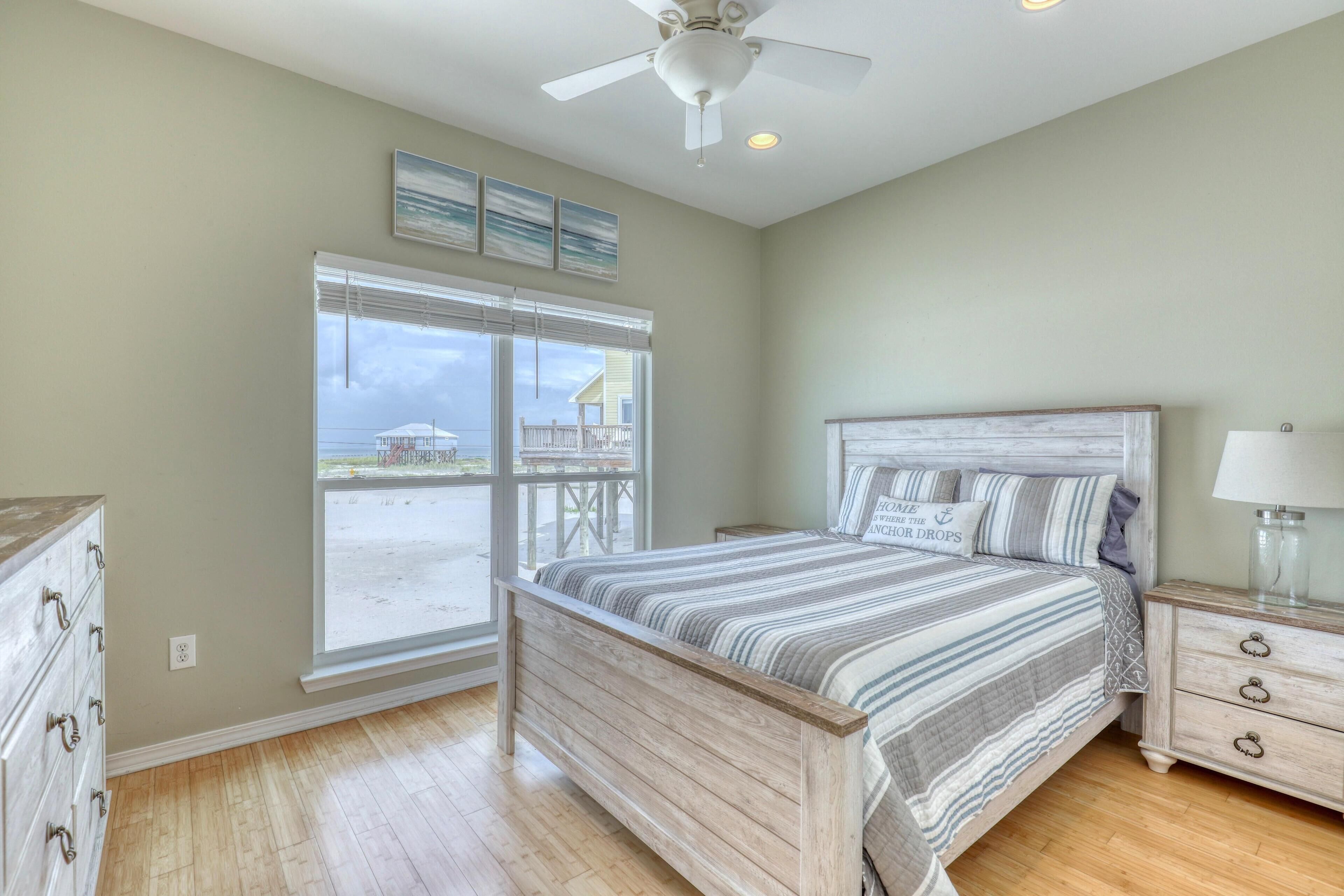 A bedroom with a large window, a bed with striped bedding, a nightstand, and a dresser.