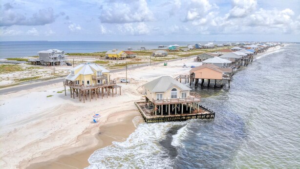 A coastal area with beachfront properties, including houses on stilts and a pier extending into the water. - Villa Delphinus - 103 Vargus C (Dauphin Island)