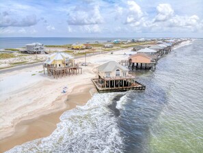 A coastal area with beachfront properties, including houses on stilts and a pier extending into the water.