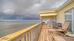 A wooden deck with a railing, a covered seating area with chairs and a table, and a view of the ocean. - Rainbows End - 100-b Shell Ct (Dauphin Island)