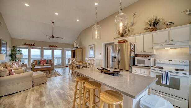 A spacious kitchen with a large island, bar stools, and modern appliances. - Rainbows End - 100-b Shell Ct (Dauphin Island)