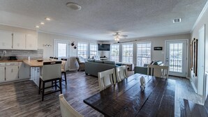 A spacious kitchen with a dining area, large windows, and a ceiling fan. - Sea Spot - 2252 Mallard (Dauphin Island)