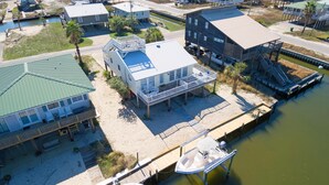 A coastal area with multiple houses, some elevated on stilts, and a dock with boats. - Sea Spot - 2252 Mallard (Dauphin Island)