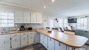 A modern kitchen with white cabinets, a wooden countertop, and a built-in TV. - Sea Spot - 2252 Mallard (Dauphin Island)