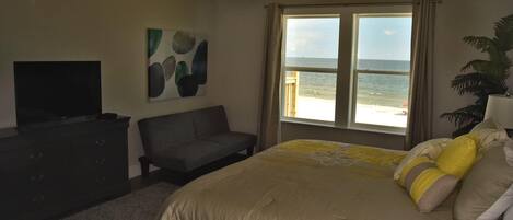 A bedroom with a bed, a TV, a sofa, and a window with a view of the beach.