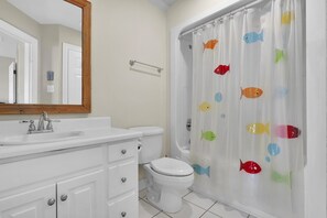 A bathroom with a white sink, a toilet, a mirror, and a shower curtain with fish patterns.
