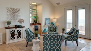 A living room with teal patterned chairs, a white cabinet, and a view of the ocean through a sliding door.