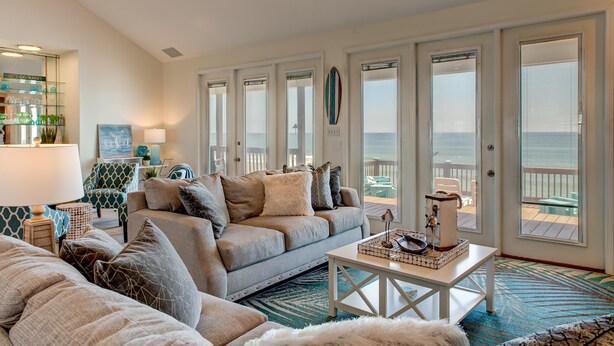 A spacious living room with a large gray sofa, a coffee table, and a view of the ocean through large windows.