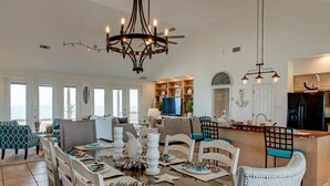 A spacious living area with a dining table set for a meal, a kitchen area with modern appliances, and a large window offering a view of the outdoors.