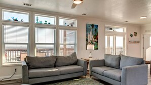 A living room with two grey sofas, a coffee table, and a large window with blinds. - Wave Loudest - 103 Pushmata (Dauphin Island)