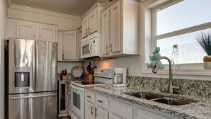 A modern kitchen with white cabinets, stainless steel appliances, granite countertops, and a window with a view. - Wave Loudest - 103 Pushmata (Dauphin Island)