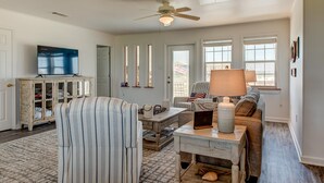 A living room with a television, a ceiling fan, a sofa, a coffee table, and a cabinet. - Saltaire - 2440 Bienville (Dauphin Island)