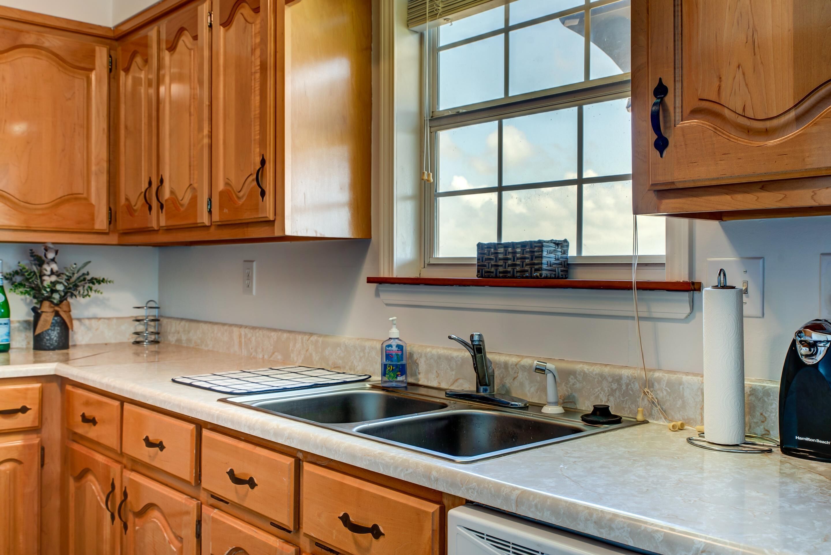A kitchen with wooden cabinets, a double sink, and a window with blinds.