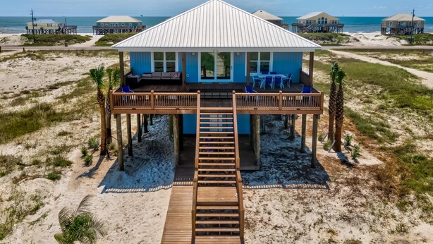 A beachfront house with a wooden deck, outdoor seating, and a staircase leading to the entrance.