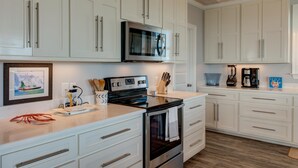 A modern kitchen with white cabinetry, stainless steel appliances, and a wooden ceiling.