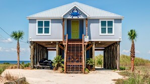 A two-story beach house with a green door, a blue crab decoration above the entrance, and a number '2432' on the right side.